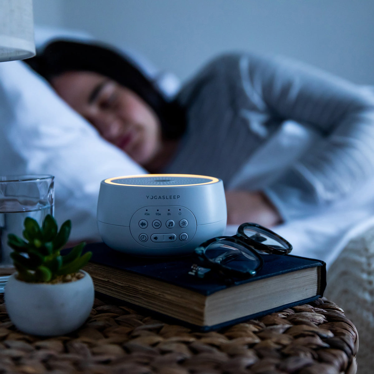 Yogasleep sound machine glowing beside a sleeping person in a bedroom