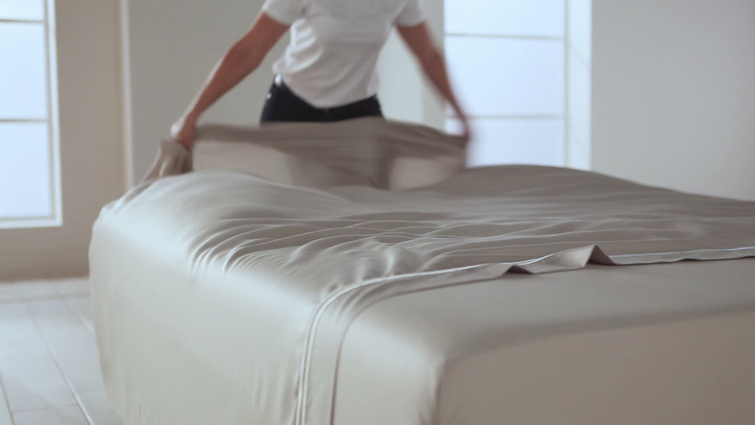 Person straightening light gray TENCEL Lyocell bed sheet in a bright bedroom setting