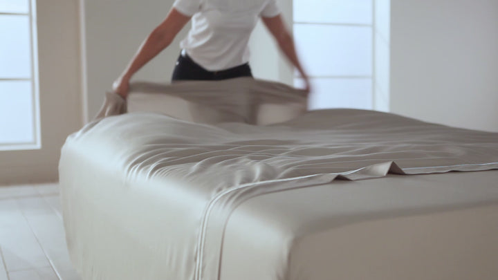 Person straightening light gray TENCEL Lyocell bed sheet in a bright bedroom setting